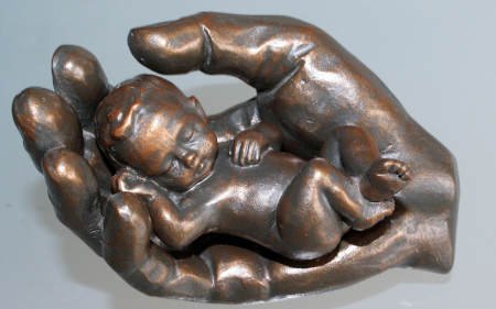 Bronzefigur: Baby geborgen in einer Hand – veranschaulicht Geborgenheit, Sicherheit und Fürsorge während der Hypnose bzw. Hypnosetherapie in meiner Praxis zentral in Mannheim, in der Oststadt nahe dem Wasserturm und dem Rosengarten.